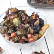 Glass bowl with roasted brussels sprouts and more sprouts on a baking tray behind it.