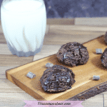 chocolate coconut drop cookies in line on a wooden cutting board with a glass of milk beside it