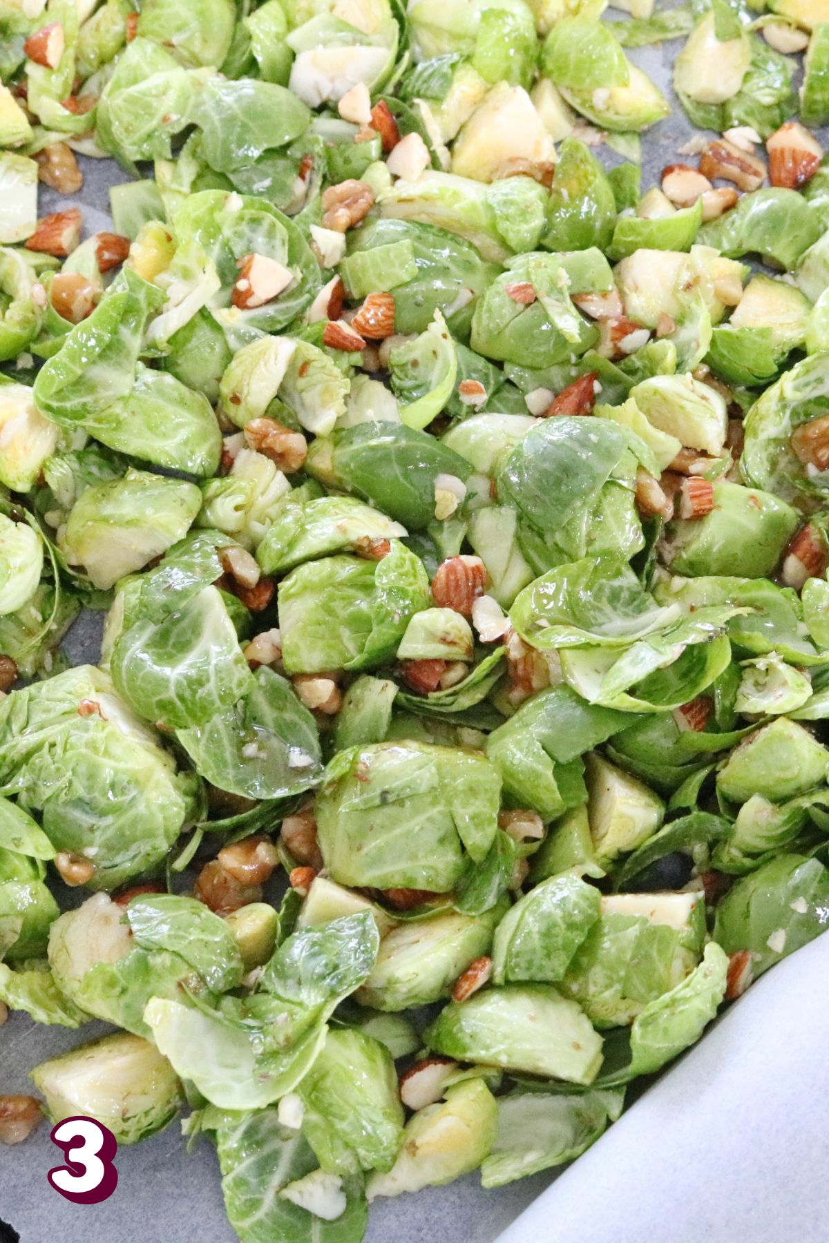 Raw brussels sprouts cooated with syrup and nuts on a baking sheet with parchment paper.