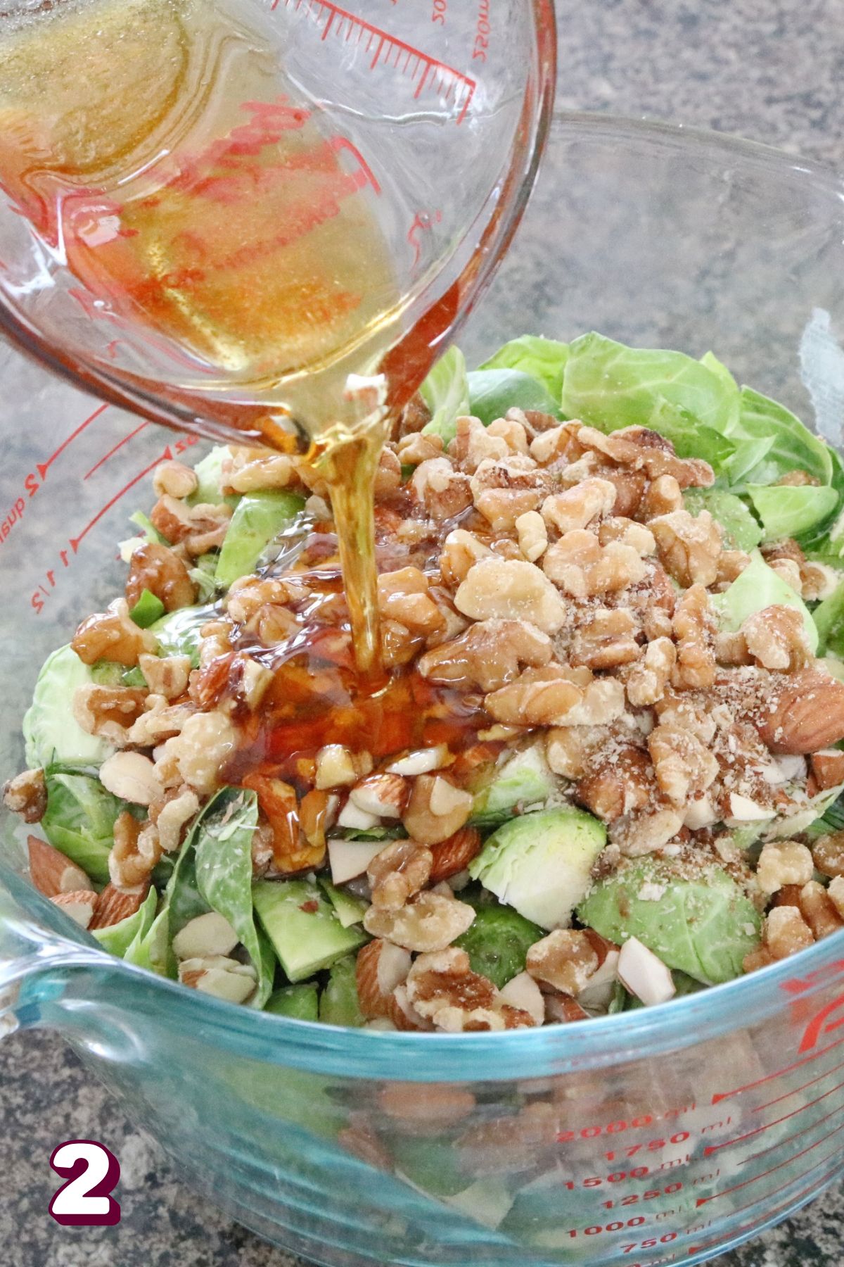 Maple syrup being poured over chopped brussel sprouts and nuts in a measuring cup.