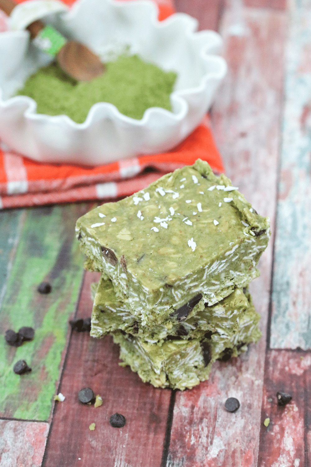 Three stacked green vegan protein bars with matchinga in a bowl on an orange napkin behind it