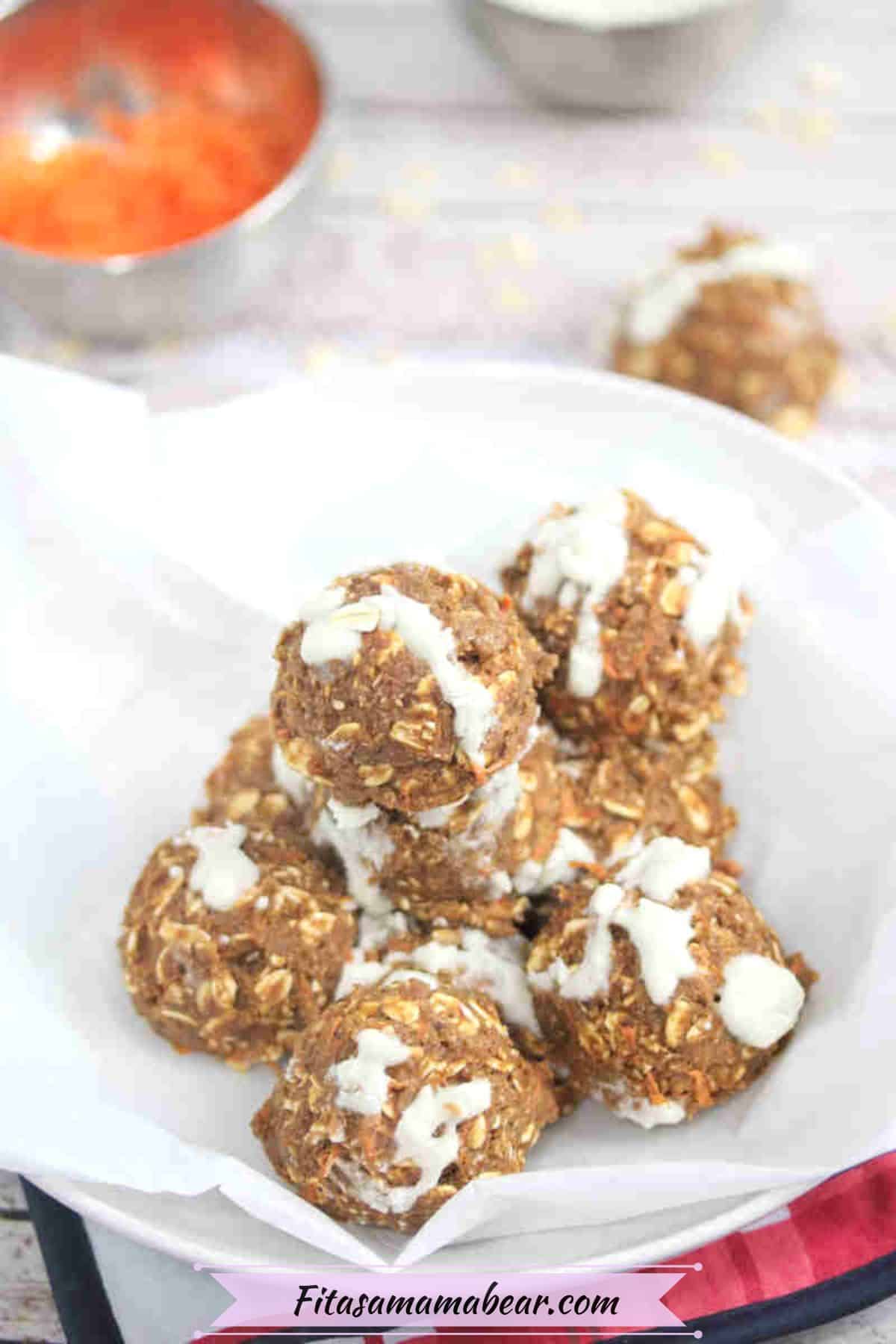 Carrot cake balls with coconut drizzle in a bowl with parchment paper and carrot in a bowl behind them.