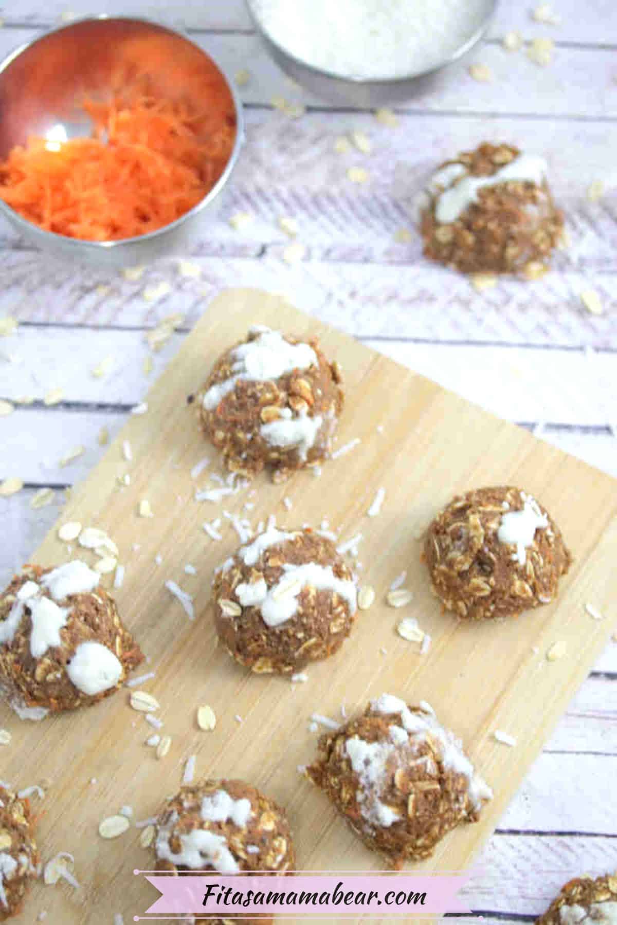 Carrot cake protein balls on a wooden cutting board with a bowl of carrot beside them and coconut and oats around them.