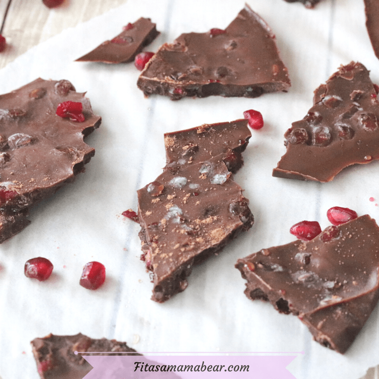 featured image with text: chocolate pomegranate bark broken up on parchment paper with pomegranate seeds around it