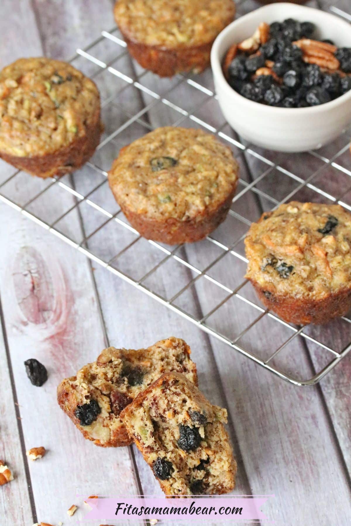 One morning glory muffin split in half with more muffins and a bowl of dried fruit on a cooling rack behind it