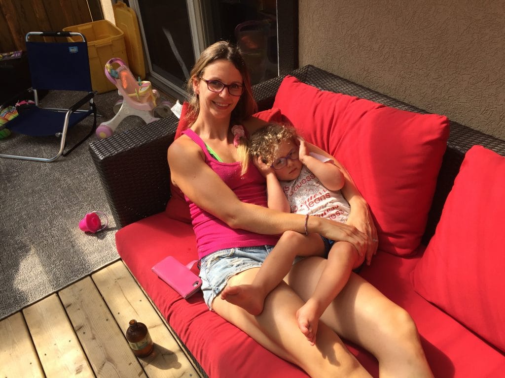 Mom and toddler snuggling together on a red couch on the deck in the sun