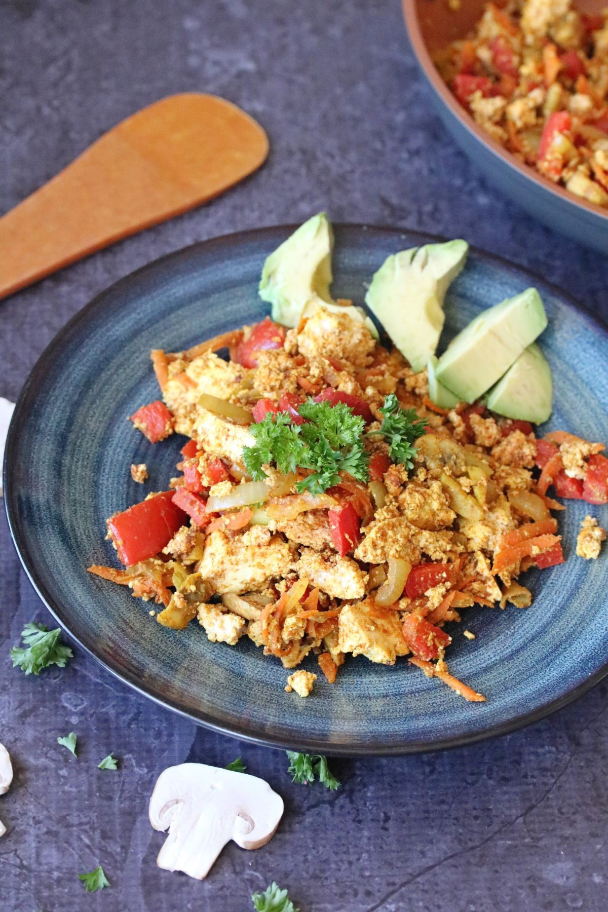 Blue plate with tofu veggie scramble on it topped with avocados.