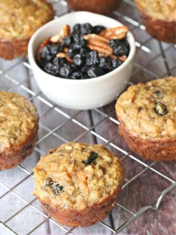Paleo morning glory muffins on a cooling rack with a bowl of dried blueberries.