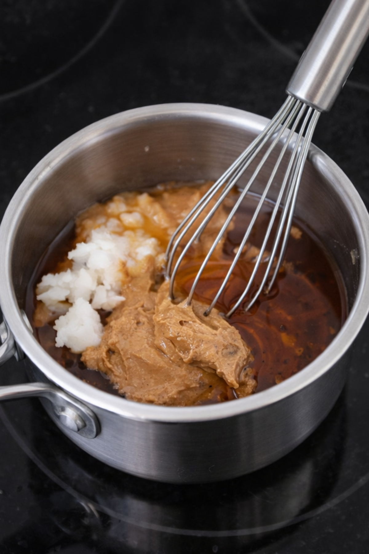 Almond butter maple syrup and coconut oil in a pot with a whisk.