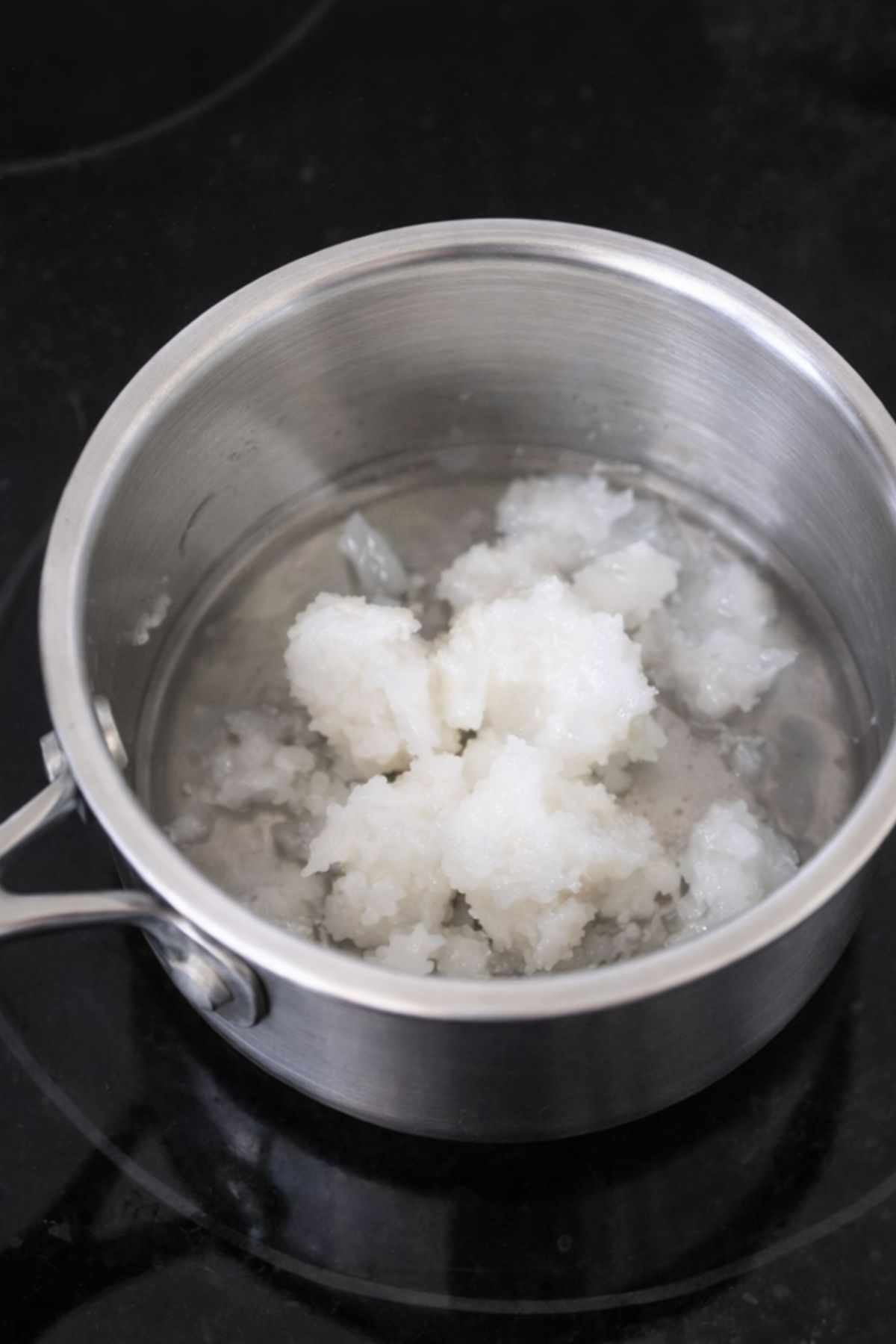 Coconut oil in a small pot on a black stove.