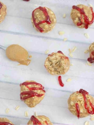 Peanut butter and jam protein balls drizzled with jam on parchment paper