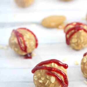 Peanut butter and jam protein balls drizzled with jam on parchment paper