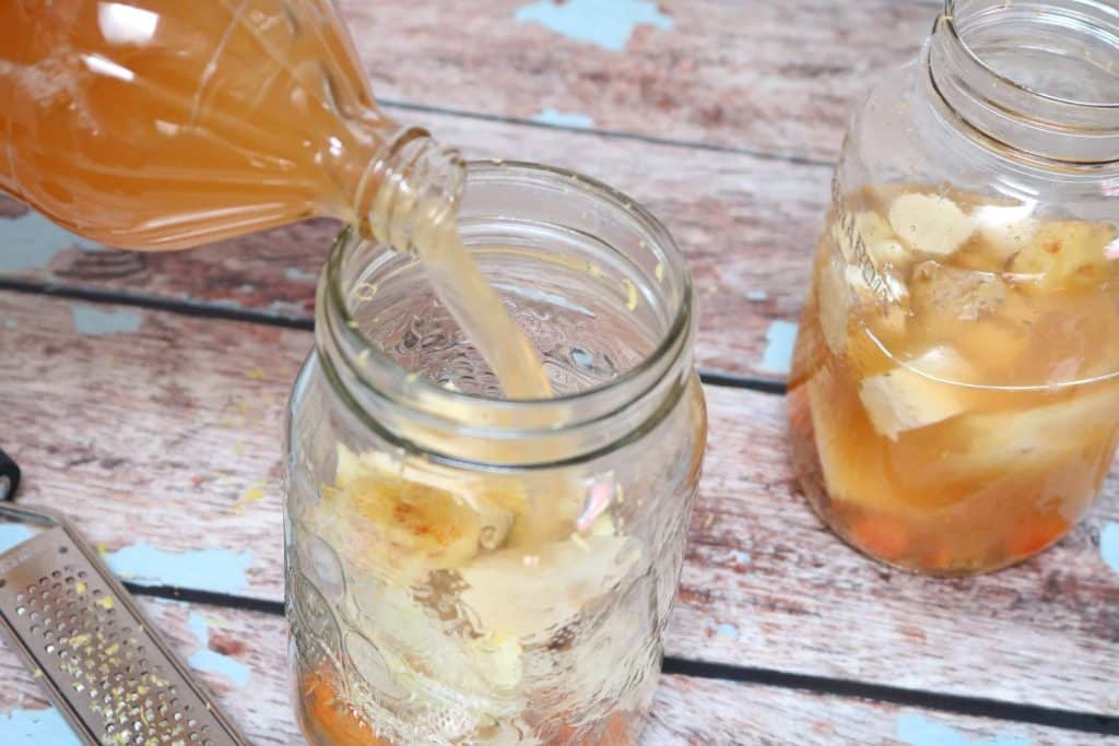 Apple cider vinegar being poured into a mason jar with raw vegetables and spices in it