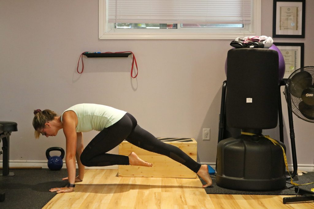 Image of a women in a light green tank top and black exercise pants doing an exercise move.