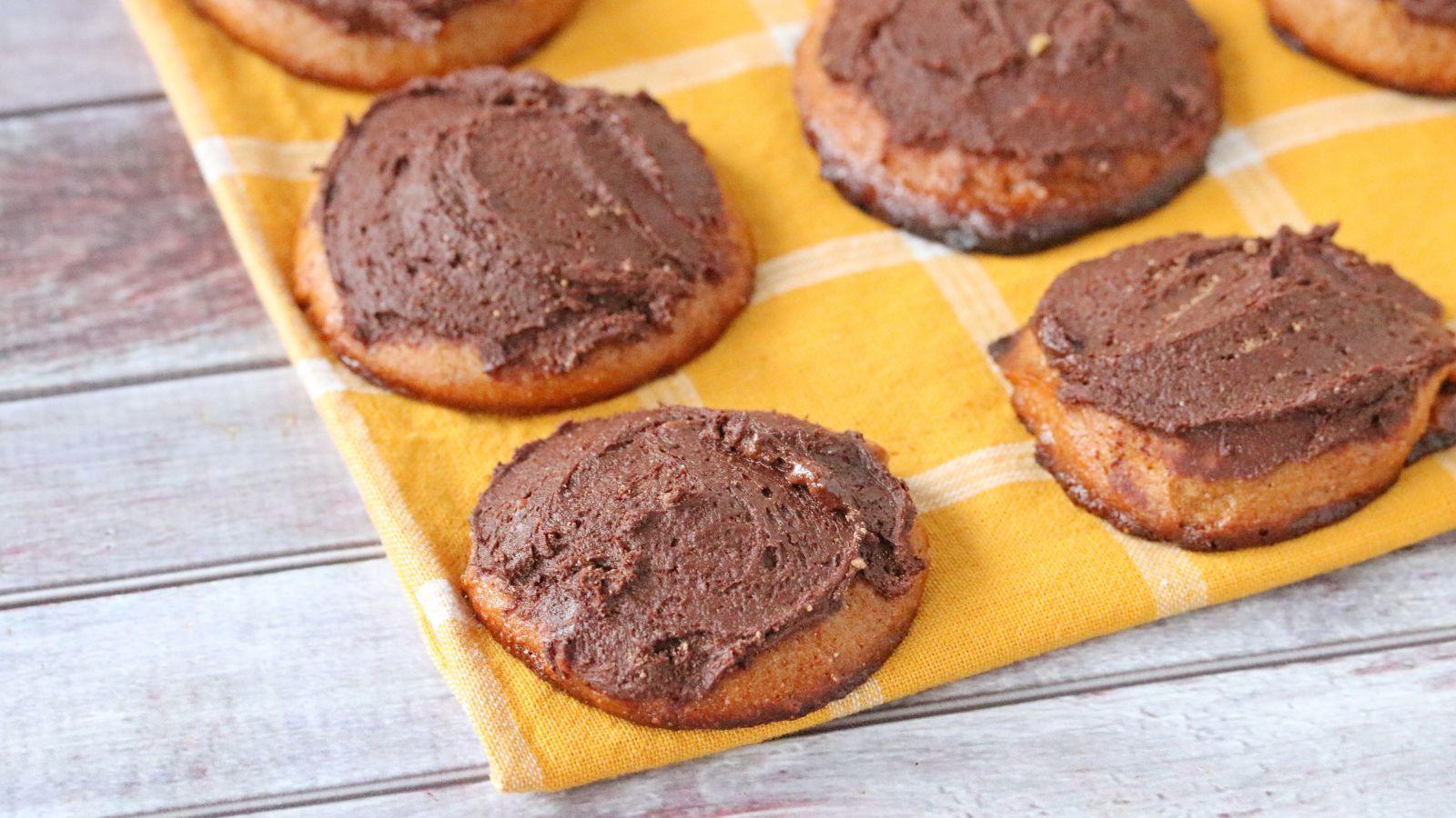 Cashew butter cookies topped with chocolate frosting in rows on a yellow linen