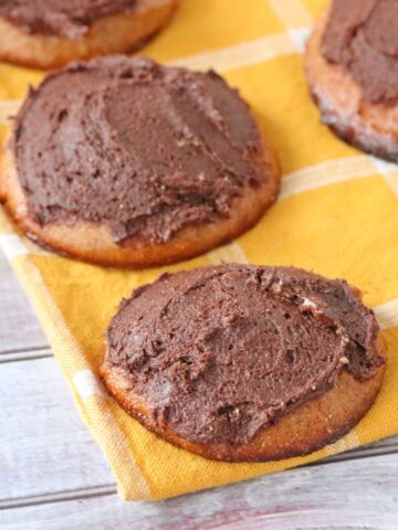 Cashew butter cookies frosted with chocolate on a yellow linen.