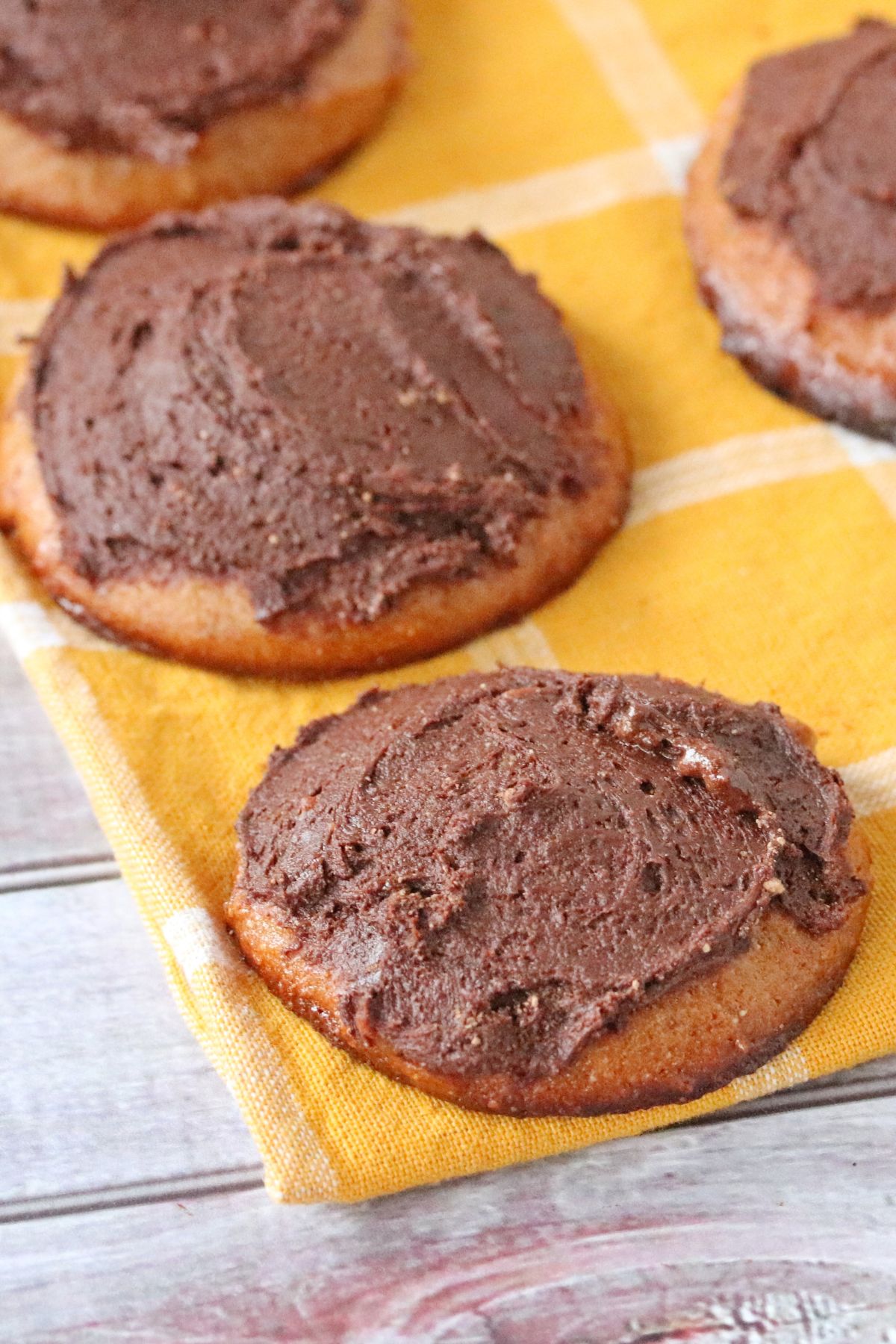Cashew butter cookies frosted with chocolate on a yellow linen.