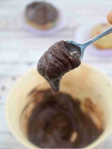 Close up of a spoon with dairy-free chocolate fosting over a bowl of more frosting.