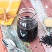 homemade elderberry syrup in a mason jar with cinnamon sticks, honey and elderberries around it