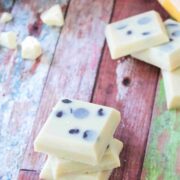 Three pieces of white dairy-free fudge stacked with cacao butter and more fudge behind them.