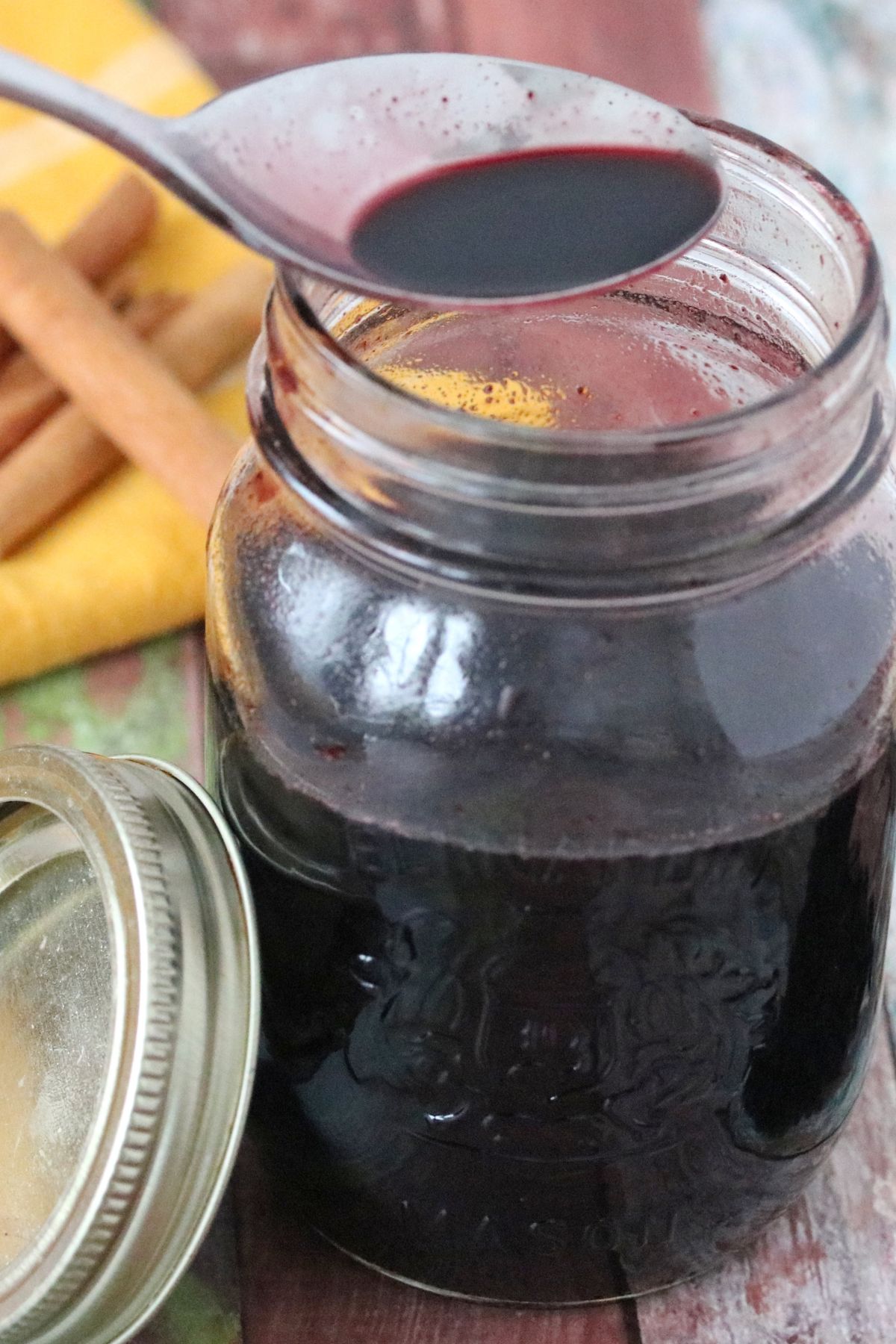 Elderberry syrup with honey in a mason jar with a spoon pulling some out.