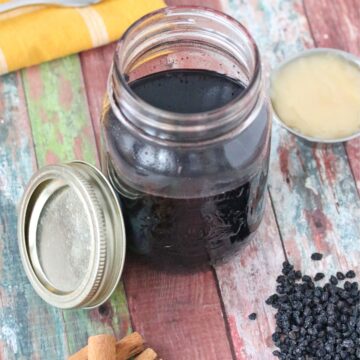 Homemade elderberry syrup in a mason jar with cinnamon sticks, honey and elderberries around it.