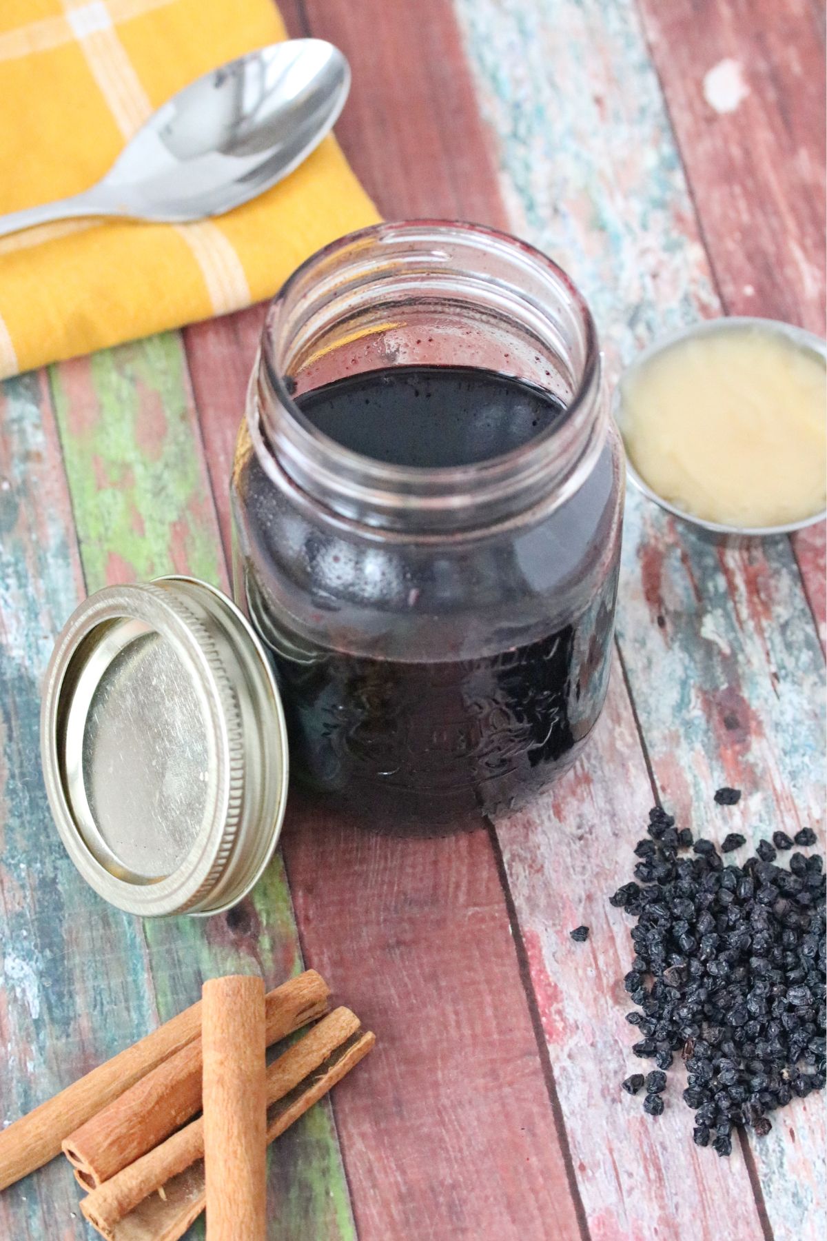 Homemade elderberry syrup in a mason jar with cinnamon sticks, honey and elderberries around it.