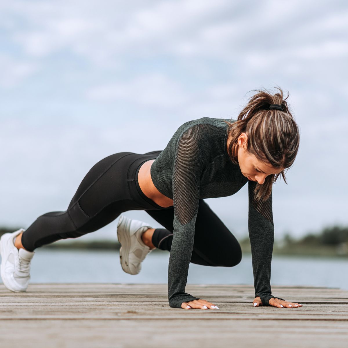 Woman outside with hands on the ground performing a mountain climber.