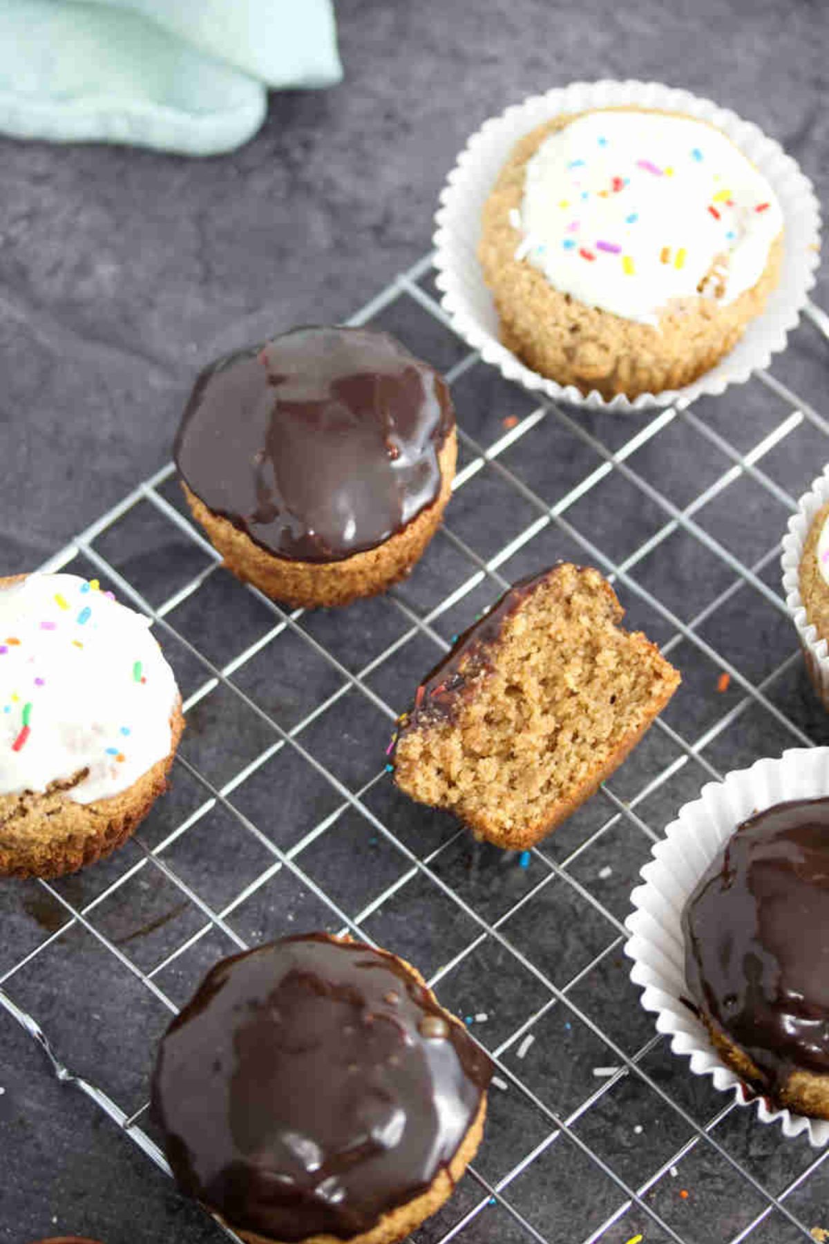 Almond flour cupcakes topped with chocolate glaze and cream cheese frosting on a cooling rack with one cupcake split in half.