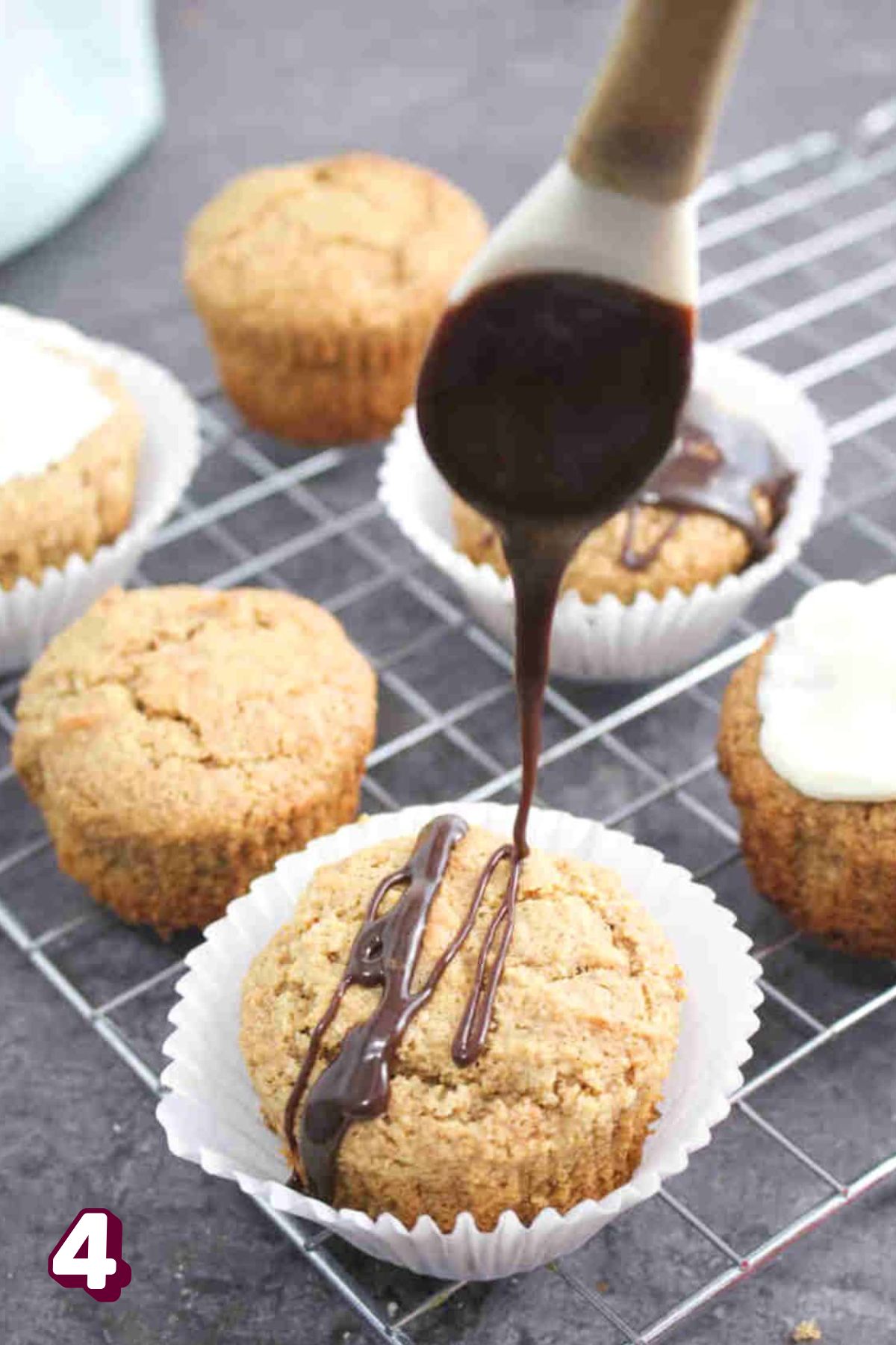 Chocolate glaze being drizzled on a vanilla gluten-free cupcake with more cupcakes on a cooling rack around it.