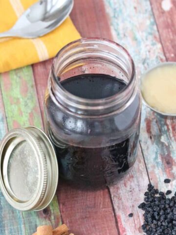 Homemade elderberry syrup in a mason jar with cinnamon sticks, honey and elderberries around it.
