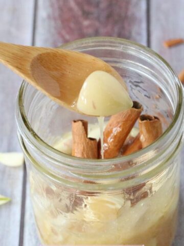 Mason jar with cinnamon, honey and garlic cloves and a wooden spoon pulling out a scoop