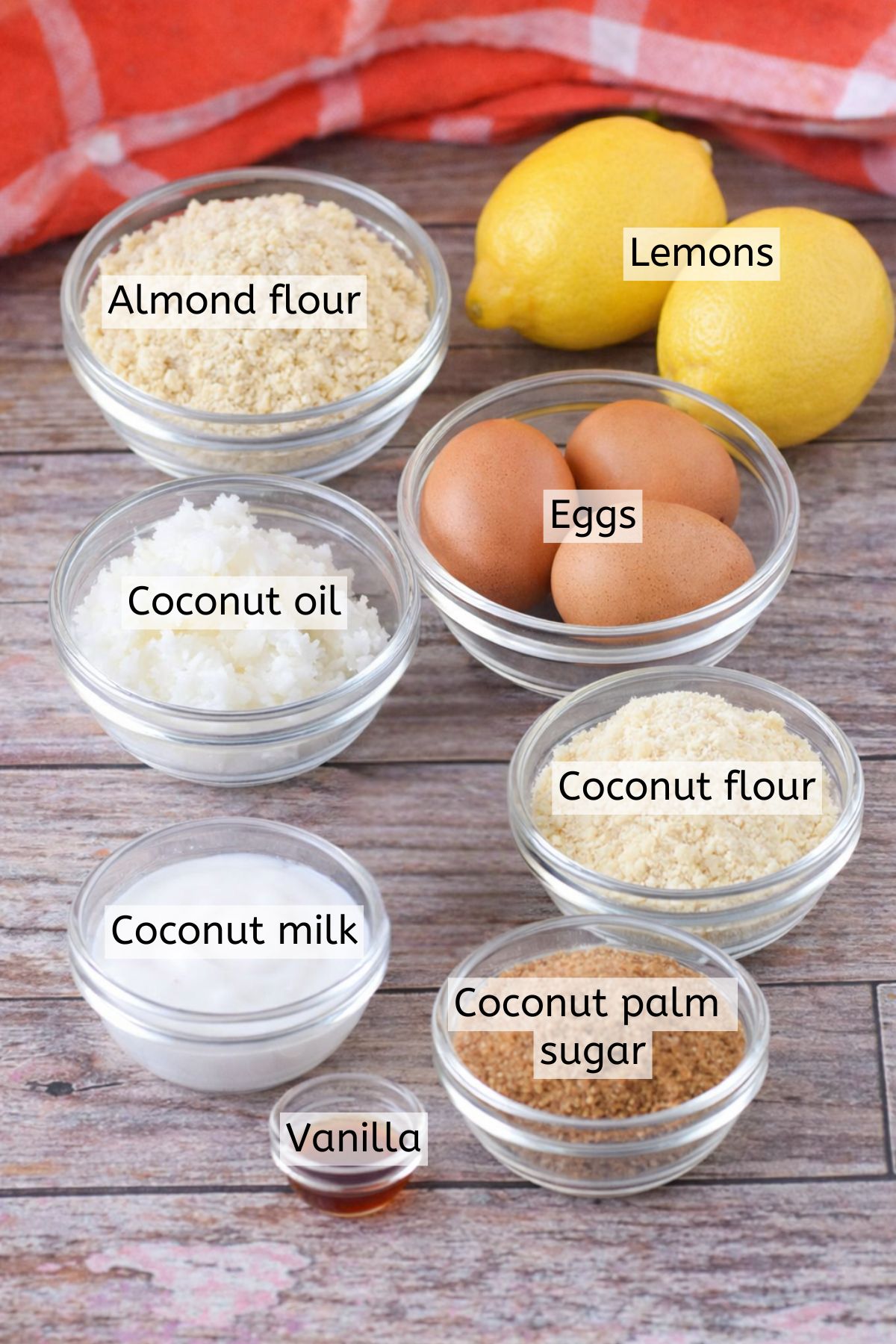 Lemons, almond flour, vanilla, eggs, and oil in glass dishes with text labels over top.