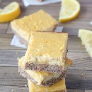 Lemon squares stacked with lemons around them. Lemons in a bowl behind them and more squares around and behind.