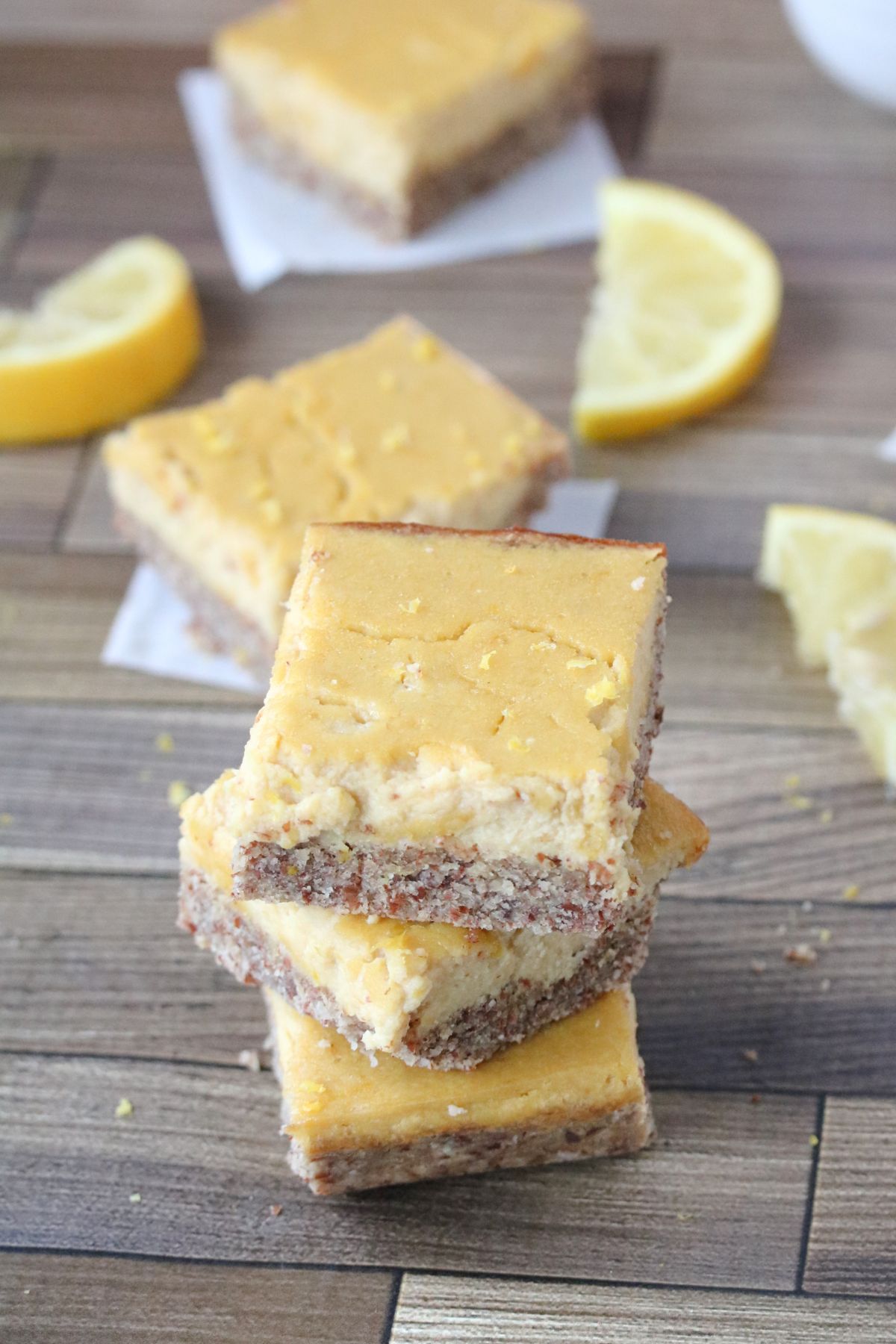 Lemon squares stacked with lemons around them. Lemons in a bowl behind them and more squares around and behind.