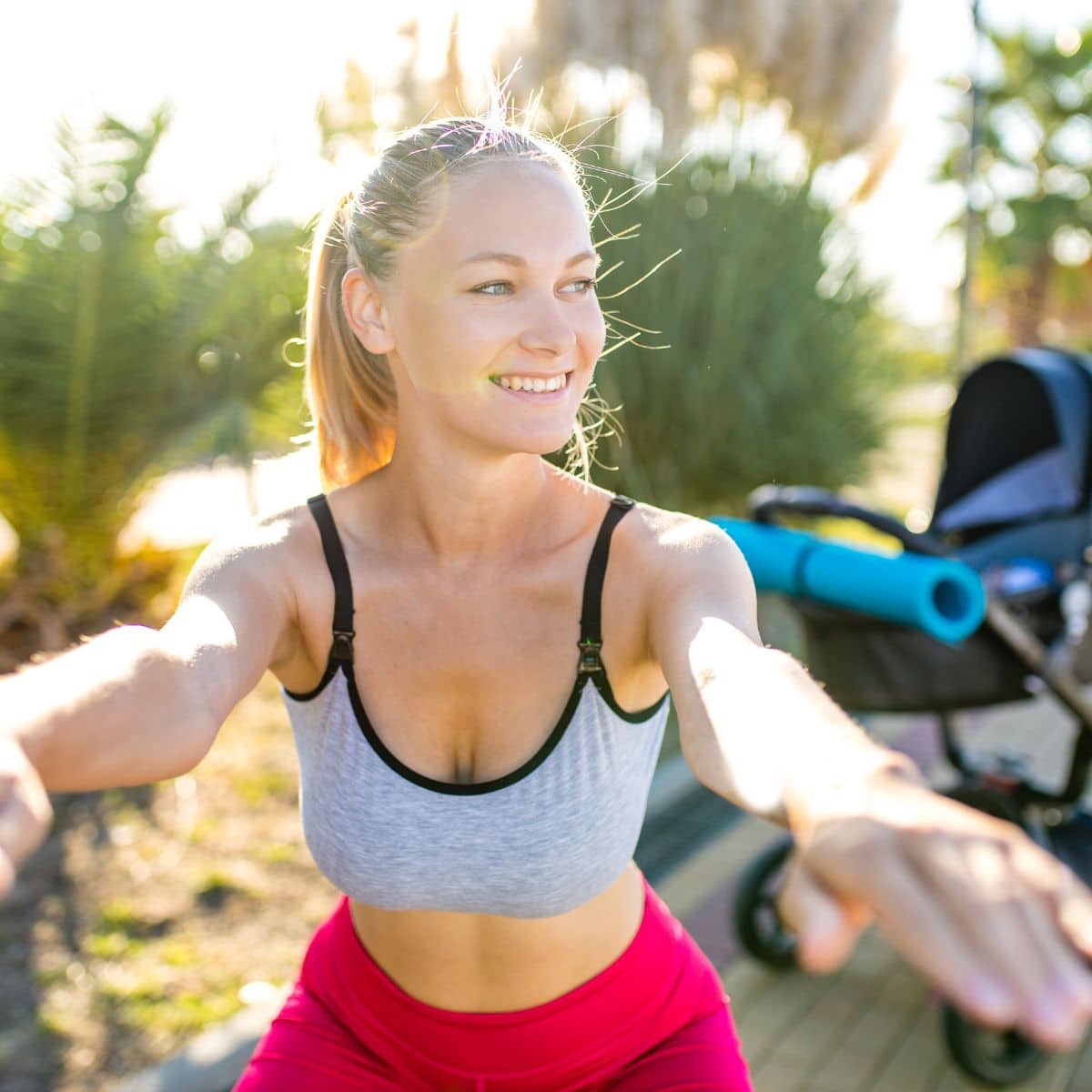 Blond hair woman working out outside with a stroller behind her