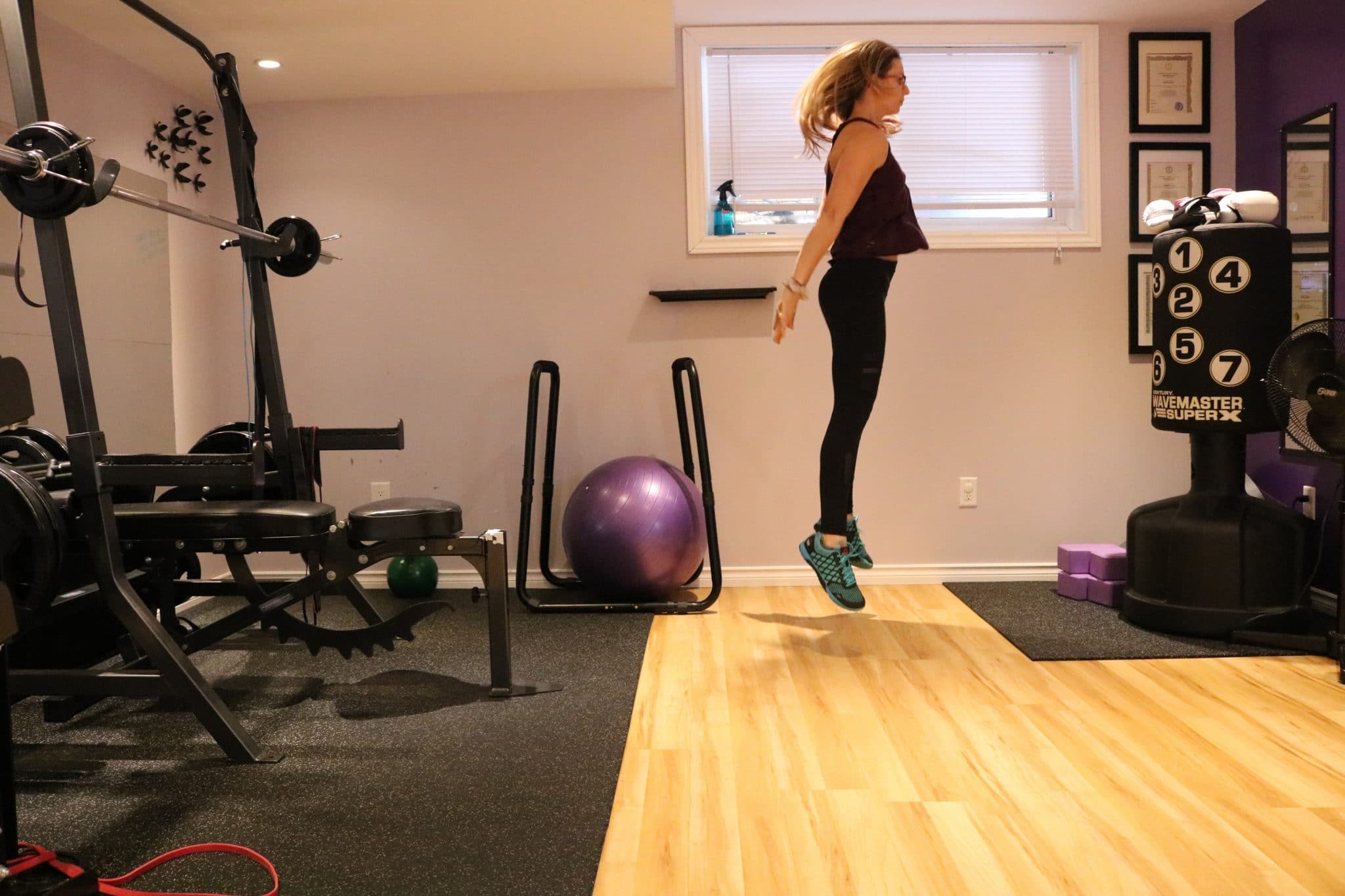 Woman in dark fitness clothes at the top of a jump in a gym