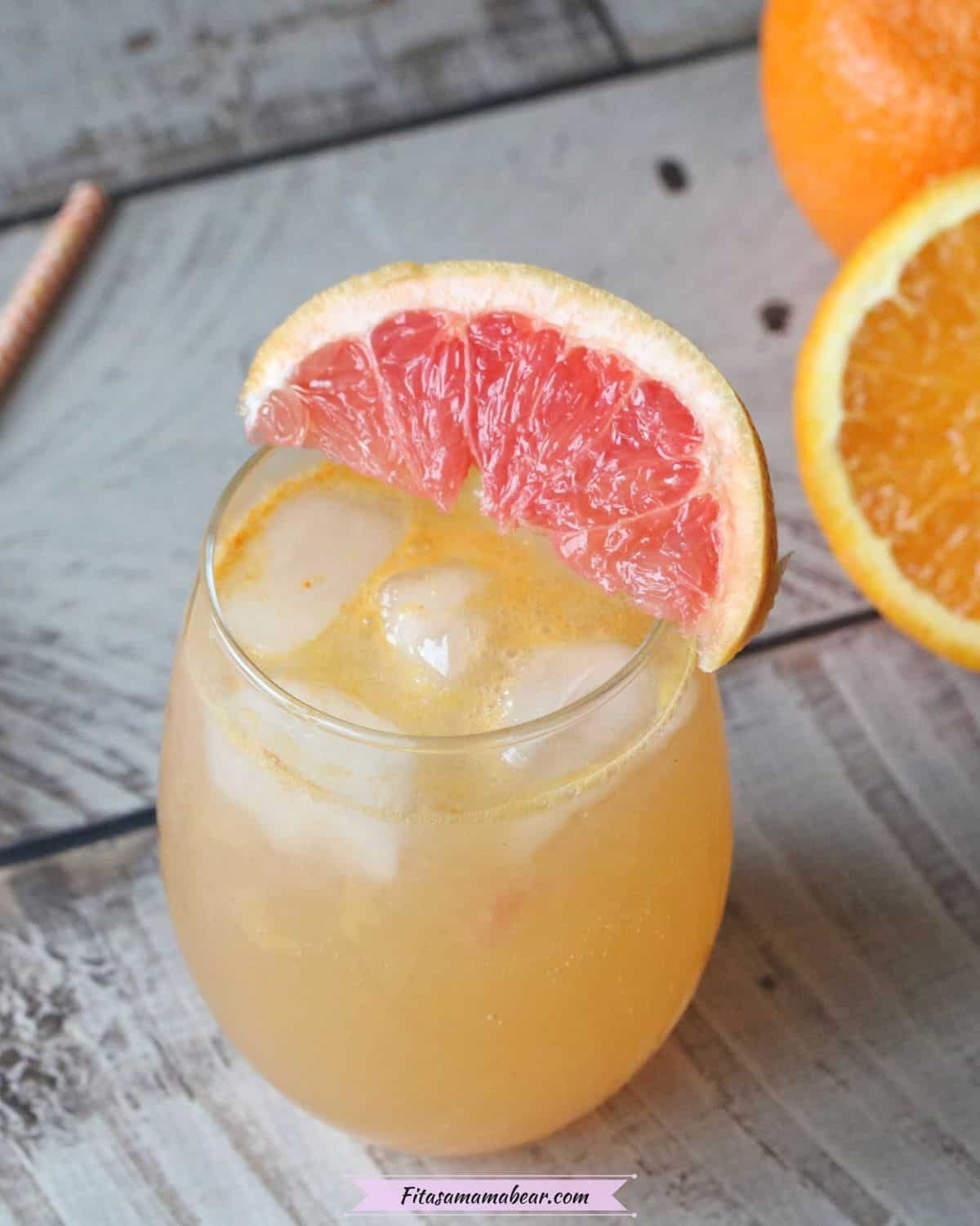 Orange mocktail in a glass with grapefruit on the rim and oranges behind it with orange straws