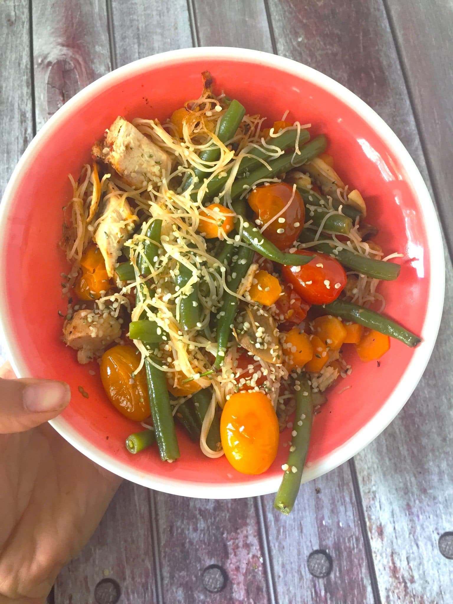 A red bowl with noodles, tomatoes and snap peas mixed together for lunch
