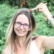 Woman outside in peach shirt using a makeup brush to distribute dry shampoo into her hair