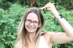 Woman outside in peach shirt using a makeup brush to distribute dry shampoo into her hair