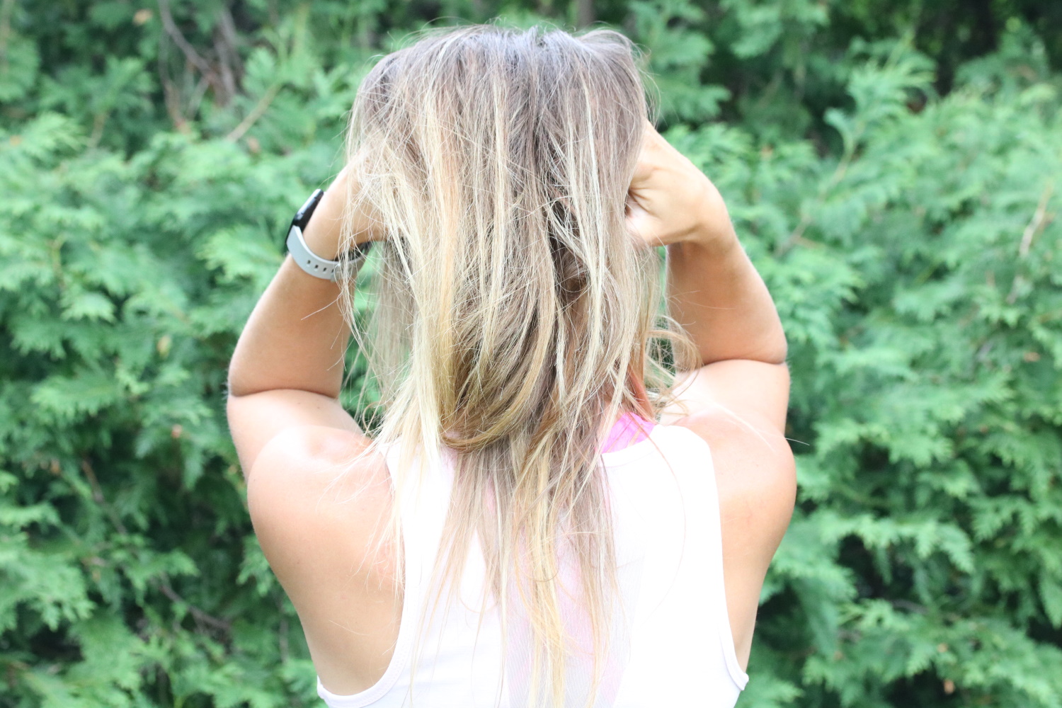 Photo of women from behind with her hands in her hair outside.