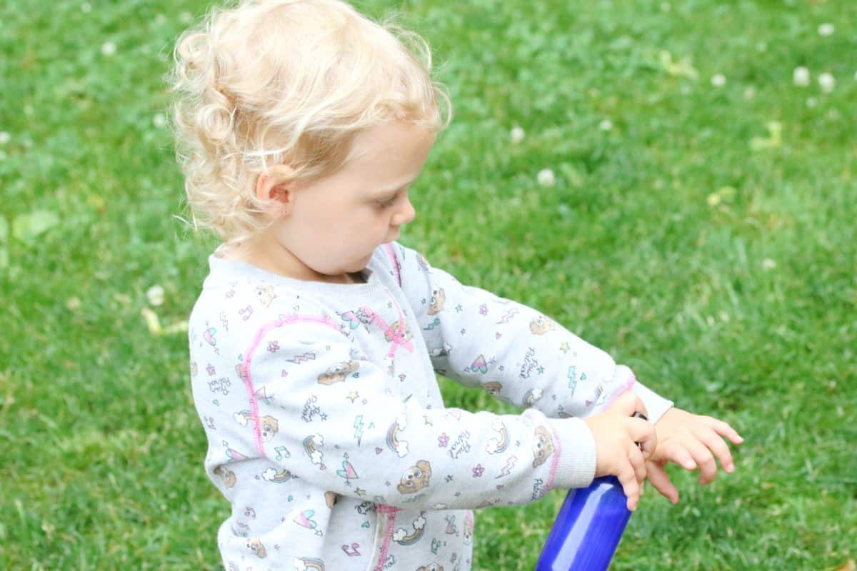 Toddler dressed in grey sweater spraying a blue glass bottle on her arm