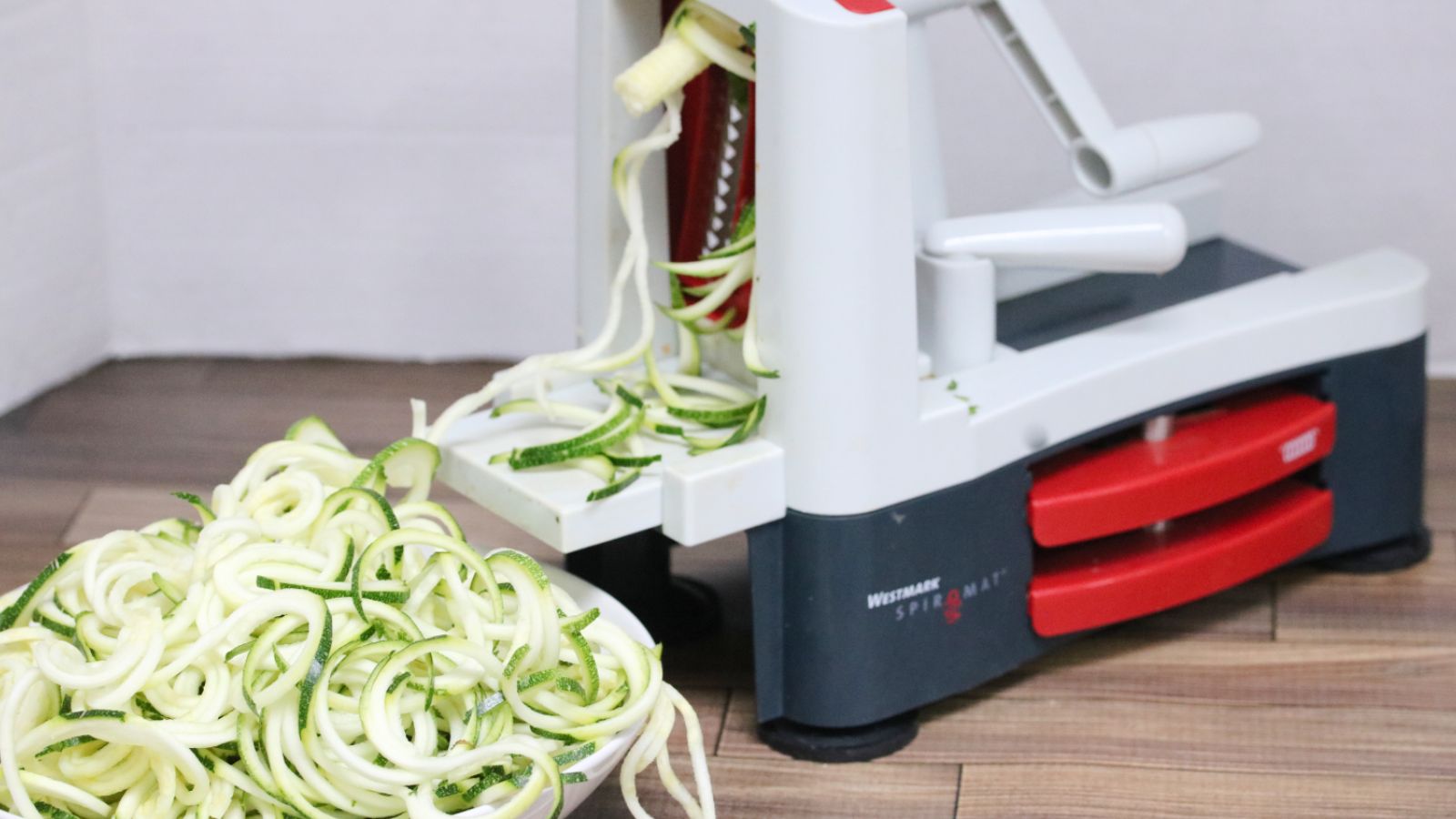 Zucchini noodles in a white bowl with a spiralizer beside it