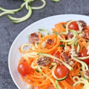 White plate with zucchini carrot salad in it with cherry tomatoes.