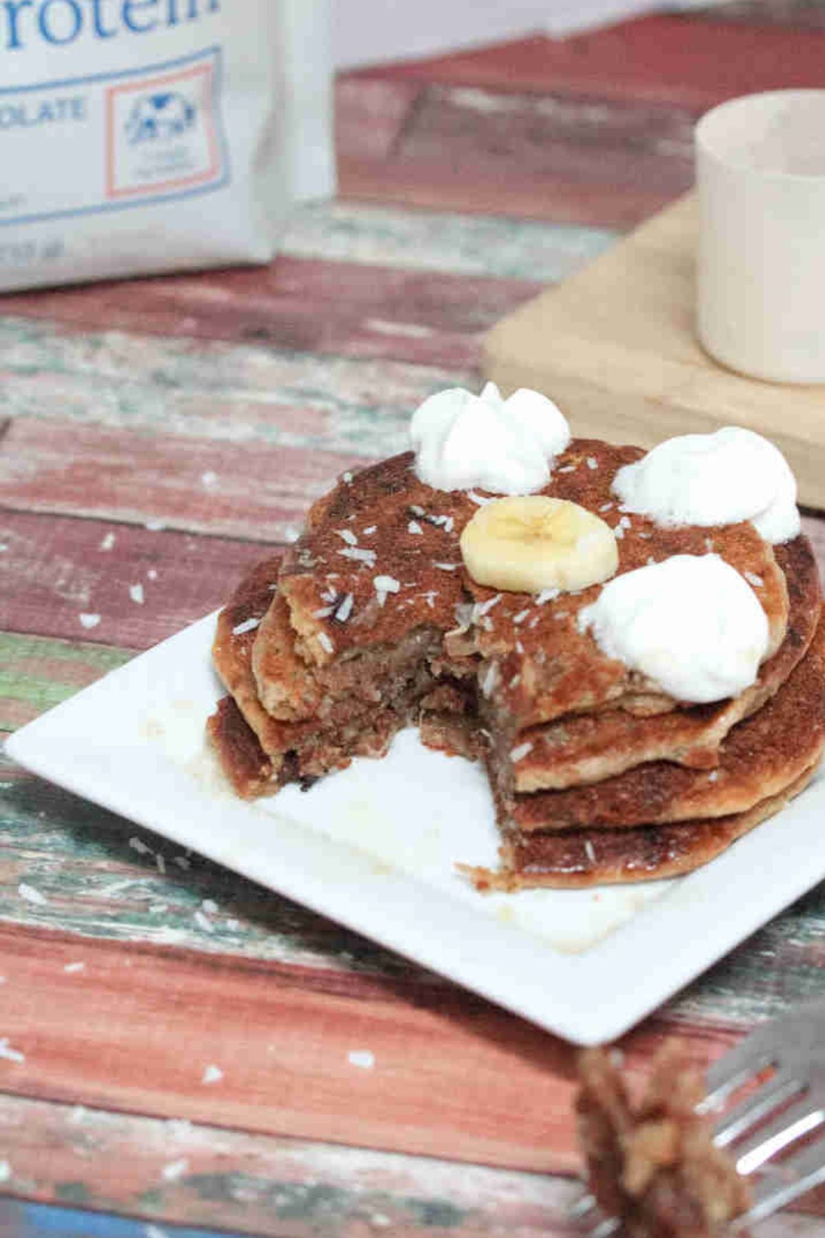 Almond flour protein pancakes stacked on white plate with banana and whipped cream on top.