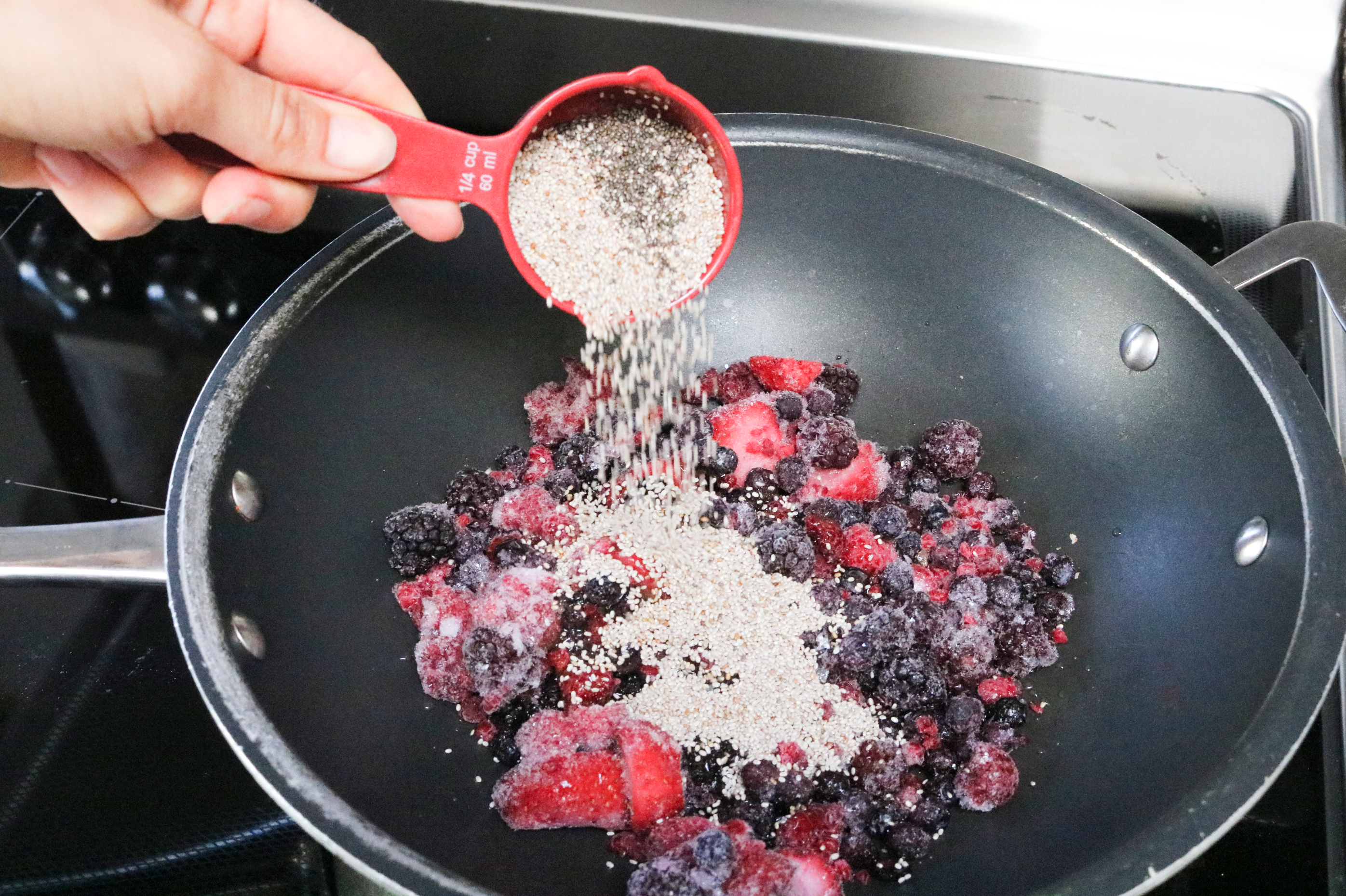 Chia seeds being poured into a wok with frozen berries