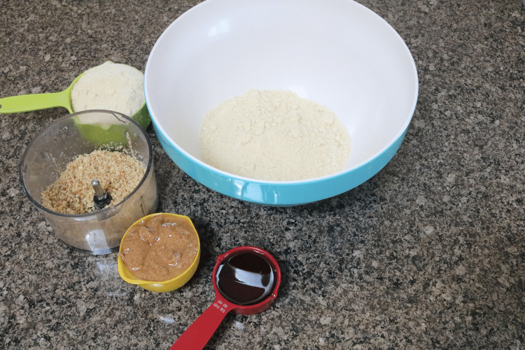 Maple syrup, nut butter and ground pecans in measuring cups beside a blue bowl
