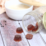 Three elderberry cough drops falling out of a tipped over mason jar with a red mold of more cough drops and a white bowl of honey behind them