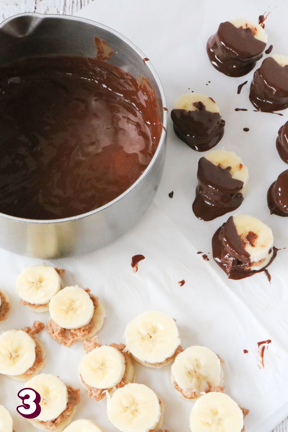 Frozen bananas with peanut butter on parchment paper, half of them dipped in chocolate.
